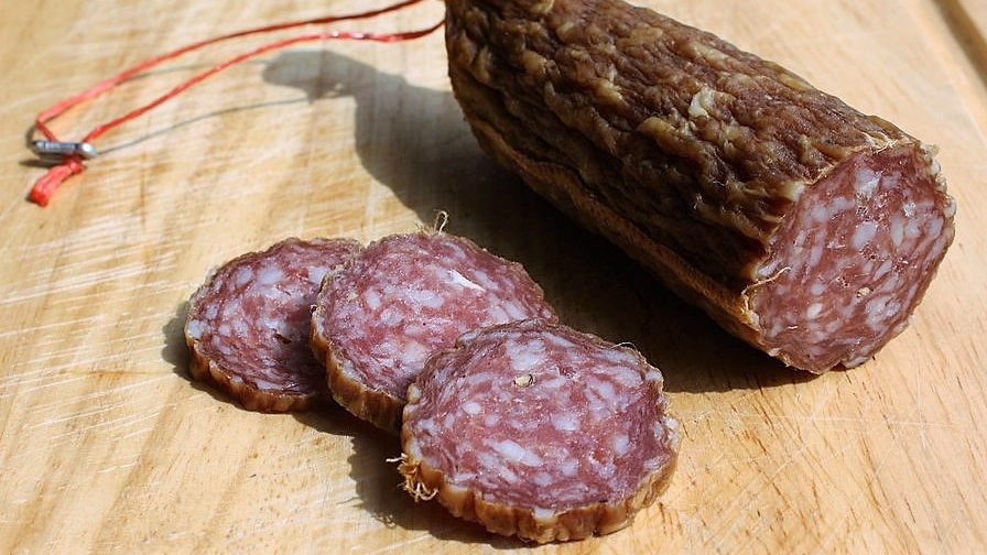 Ahle Wurst auf einem Holzbrett. Drei Scheiben sind davon abgeschnitten.