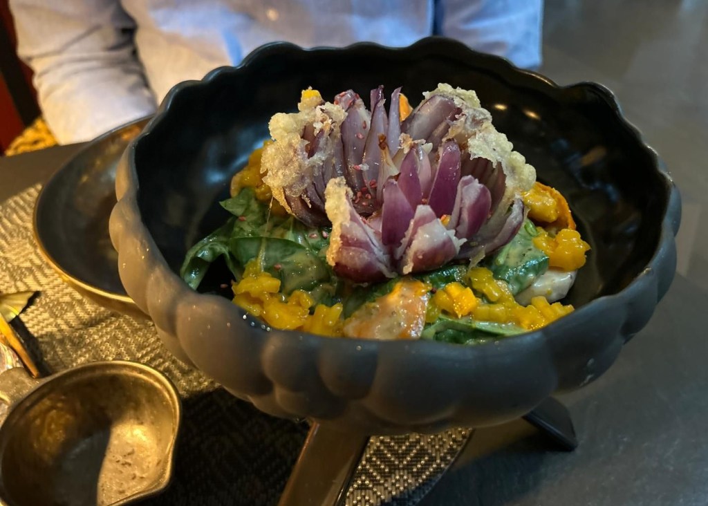 Vorspeisensalat mit einer frittierten Zwiebel in der Mitte in Form einer Blume